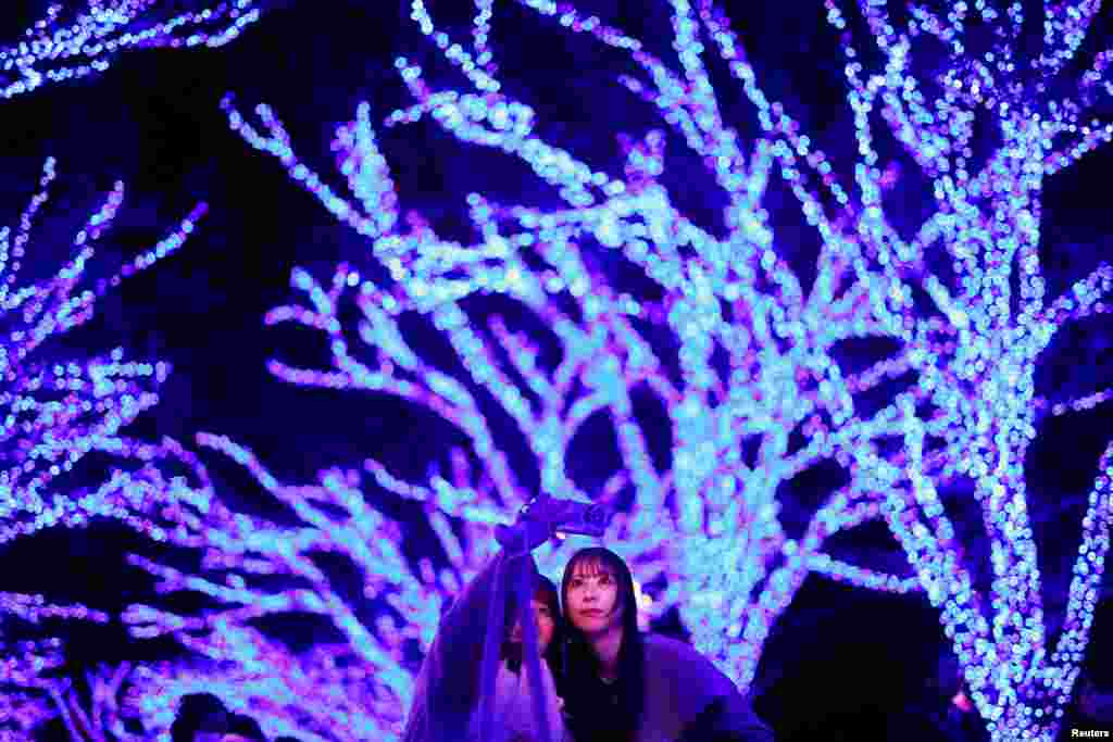 Visitors take selfie photos under Zelkova trees, lit up with blue LEDs during an illumination event called &quot;Ao no Dokutsu,&quot; or Blue Cave, to celebrate the Christmas season at Shibuya district in Tokyo, Japan.