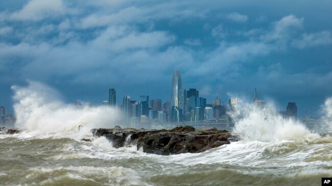 Waves crash over a breakwater in Alameda, California with the San Francisco skyline in the background on February 4, 2024. High winds and heavy rainfall are impacting the region. (AP Photo/Noah Berger)