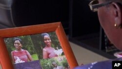 In this image taken from video, Margaret Ntale, whose three student daughters are stranded in Wuhan, China, looks at photographs of her children at her house in Kampala, Uganda, Feb. 27, 2020.