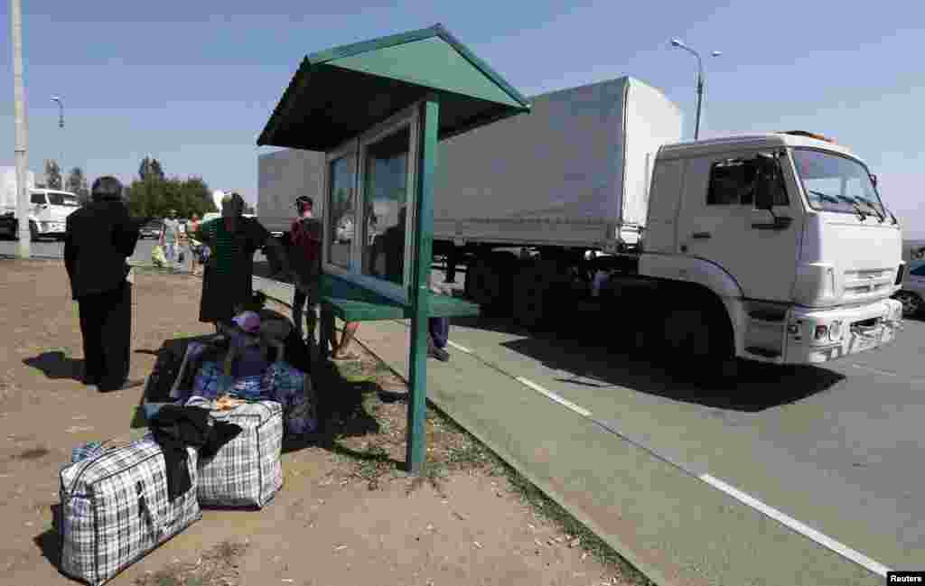 A Russian convoy carrying humanitarian aid for Ukraine drives to the Russia-Ukraine border crossing point while Ukraine refugees stand nearby, in Rostov region, Russia, Aug. 22, 2014.