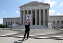 FILE - Demonstrator Bill Christeson holds a sign outside the U.S. Supreme Court, where justices ruled that a prosecutor in New York City can obtain President Donald Trump's financial records, including tax returns, in Washington, July 9, 2020.