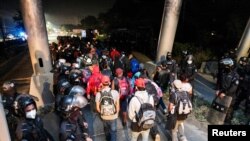 Hondureños que participan en una nueva caravana de migrantes, que se dirigirá a Estados Unidos, pasan por un puesto de control policial después de mostrar sus identificaciones a los oficiales de policía, en San Pedro Sula, Honduras, 14 de enero de 2021.