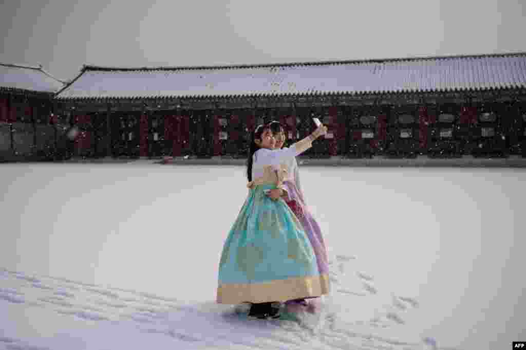 Visitors wearing traditional hanbok dress pose for selfie photos in the snow at Gyeongbokgung palace in Seoul, South Korea.