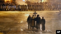 Orthodox priests pray as they stand between pro-EU protesters and police lines in central Kyiv, Jan. 24, 2014. 