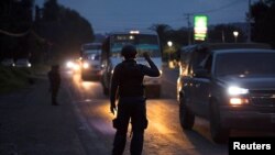 FILE - A police officer holds a flashlight during inspections at a checkpoint after 13 people were killed in battles between rival gangs in two states in central and western Mexico, Uruapan, in the state of Michoacan, Mexico, Sept. 13, 2017.