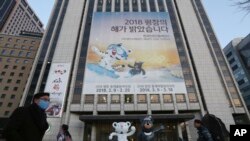 Para pejalan kaki melewati poster Olimpiade Musim Dingin 2018 Pyeongchang dan maskot olimpiade, macan putih 'Soohorang' dan beruang hitam "Bandabi" untuk paralimpik di pusat Kota Seoul, Korea Selatan, 9 Januari 2018. 