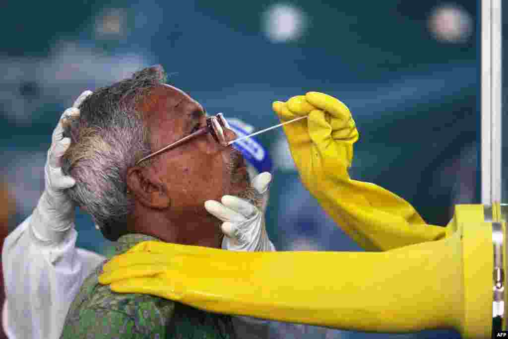 An employee of the Mugda Medical College and Hospital collects a swab sample from a resident to test for COVID-19, in Dhaka, Bangladesh.
