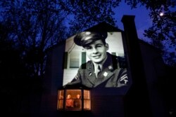 An image of veteran James Sullivan is projected onto the home of his son, Tom Sullivan, left, as he looks out a window with his brother, Joseph Sullivan, in South Hadley, Mass., May 4, 2020.