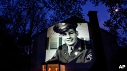 An image of veteran James Sullivan is projected onto the home of his son, Tom Sullivan, left, as he looks out a window with his brother, Joseph Sullivan, in South Hadley, Mass., May 4, 2020.