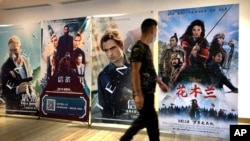FILE - A man wearing a face mask walks past a poster for the Disney movie "Mulan" at a movie theater in Beijing, on Sept. 11, 2020. 