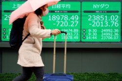 A woman walks past an electronic stock board showing Japan's Nikkei 225 index and NY Dow at a securities firm in Tokyo, March 10, 2020.