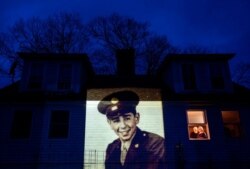 An image of veteran Emilio DiPalma, is projected onto the home of his daughter, Emily Aho, left, as she looks out a window with her husband, George, in Jaffrey, N.H., April 30, 2020.