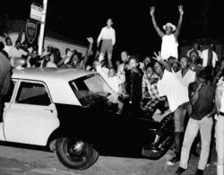 FILE - Demonstrators push against a police car in the Los Angeles neighborhood of Watts, Aug. 12, 1965.