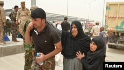 A tribal fighter helps civilians on the outskirts of Falluja, Iraq, June 18, 2016. Iraqi government-run camps struggled to shelter people fleeing Falluja, as the military battled Islamic State militants in the city's northern districts.