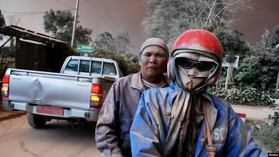 Warga dengan wajah kotor karena abu mengendarai sepeda motor di tengah muntahan abu dari Gunung Sinabung, di desa Sukandebi di Kabupaten Karo, Sumatra Utara (13/6). (Reuters/Antara/Rony Muharman)
