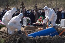 Grave diggers wearing protective suits bury a COVID-19 victim as relatives and friends stand at a safe distance, in the special purpose for coronavirus victims section of a cemetery in Kolpino, outside St. Petersburg, Russia, May 10, 2020.