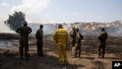 Israeli soldiers and a firefighter examine a fire started by an incendiary device launched from the Gaza Strip, on the Israeli side of the border between Israel and Gaza, near Kibbutz Netiv Ha'asara, Aug. 12, 2020. 