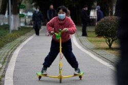FILE - A child wearing a mask rides on a skate scooter in Wuhan in central China's Hubei province, Jan. 29, 2021.