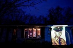 An image of veteran Francis Foley is projected onto the home of his wife, Dale Foley, left, as she looks out a window with their daughter, Keri Rutherford, in Chicopee, Mass., April 29, 2020.
