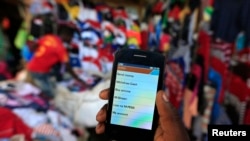 FILE - A man holds up his mobile phone at an open-air market in Kibera in Kenya's capital, Nairobi, Dec. 31, 2014.