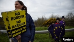 FILE - A woman carries signs as children hold an EU flag as they attend a protest against Brexit on the border crossing between the Republic of Ireland and Northern Ireland in Carrickcarnon, Ireland, March 30, 2019.