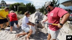 Walker Townsend (derecha), de Isle of Palms, Carolina del Sur, llena un saco de arena que sostiene Dalton Trout, en un estacionamiento municipal donde se reparte arena de forma gratuita dentro de los preparativos para la llegada del huracán Florence a la región, el 10 de septiembre de 2018. (AP Foto/Mic Smith)