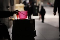 A homeless panhandler in New York City checks his bucket for money along Wall Street where much of the Financial District stands empty as the coronavirus keeps financial markets and businesses mostly closed, April 20, 2020.
