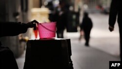 FILE - A homeless panhandler checks his bucket for money along Wall Street where much of the Financial District stands empty as the coronavirus keeps financial markets and businesses mostly closed on April 20, 2020, in New York City. 