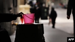 FILE - A homeless panhandler checks his bucket for money along Wall Street where much of the Financial District stands empty as the coronavirus keeps financial markets and businesses mostly closed on April 20, 2020, in New York City. 
