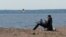 Seorang pria bekerja dengan menggunakan smartphone dan laptopnya, sambil duduk di pantai Teluk Finlandia di tengah pandemi Covid-19 di Saint Petersburg, Rusia, 27 Mei 2020. (REUTERS / Anton Vaganov)