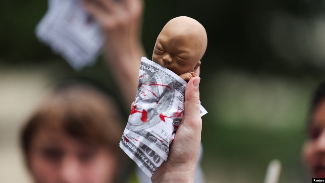 Seorang pegiat antiaborsi mengangkat alat peraga yang menggambarkan janin yang dibungkus dengan uang seratus dolar palsu di Milwaukee, Wisconsin, AS, 15 Juli 2024, sebagai ilustrasi. (Foto: REUTERS/Shannon Stapleton)