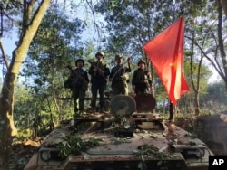 Members of the resistance Myanmar National Democratic Alliance Army hold the group's flag as they pose for a photograph on a captured army armored vehicle in Myanmar on Oct. 28, 2023.