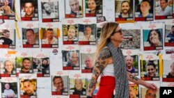 FILE - A woman walks past pictures of hostages in Tel Aviv, Israel, Februry 12, 2024. The Israeli military has rescued two hostages from captivity in the Gaza Strip.