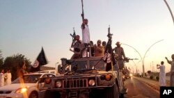 FILE - Fighters from the Islamic State group parade in a commandeered armored vehicle down a main road at the northern city of Mosul, Iraq.