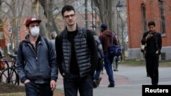 FILE - A student wearing a mask to protect against the coronavirus walks with others at Harvard University, before the school moved its classes to online-only, in Cambridge, Massachusetts, March 10, 2020.