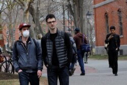 FILE - A student wearing a mask to protect against the coronavirus walks with others at Harvard University, before the school moved its classes to online-only, in Cambridge, Massachusetts, March 10, 2020.