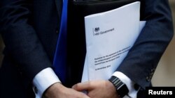 FILE - Conservative Party politician Steve Baker holds a Brexit document as British Member of Parliament, Jacob Rees-Mogg, speaks from St Stephen's Entrance at the Houses of Parliament, in London, Nov. 15, 2018. 