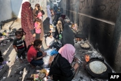 Para perempuan duduk membuat roti pipih tradisional di sepanjang gang di Rafah di Jalur Gaza selatan pada 1 November 2023 di tengah pertempuran yang sedang berlangsung antara Israel dan Hamas. (Foto: AFP)