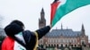 Seorang pria mengibarkan bendera Palestina ketika massa melakukan demonstrasi pada hari sidang publik yang diadakan oleh Mahkamah Internasional (ICJ) di Den Haag, Belanda, 21 Februari 2024. (Foto: Reuters)
