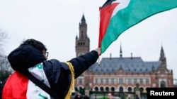 Seorang pria mengibarkan bendera Palestina di depan Gedung Mahkamah Internasional (ICJ) di Den Haag, Belanda, 21 Februari 2024. (Foto: REUTERS/Piroschka van de Wouw)