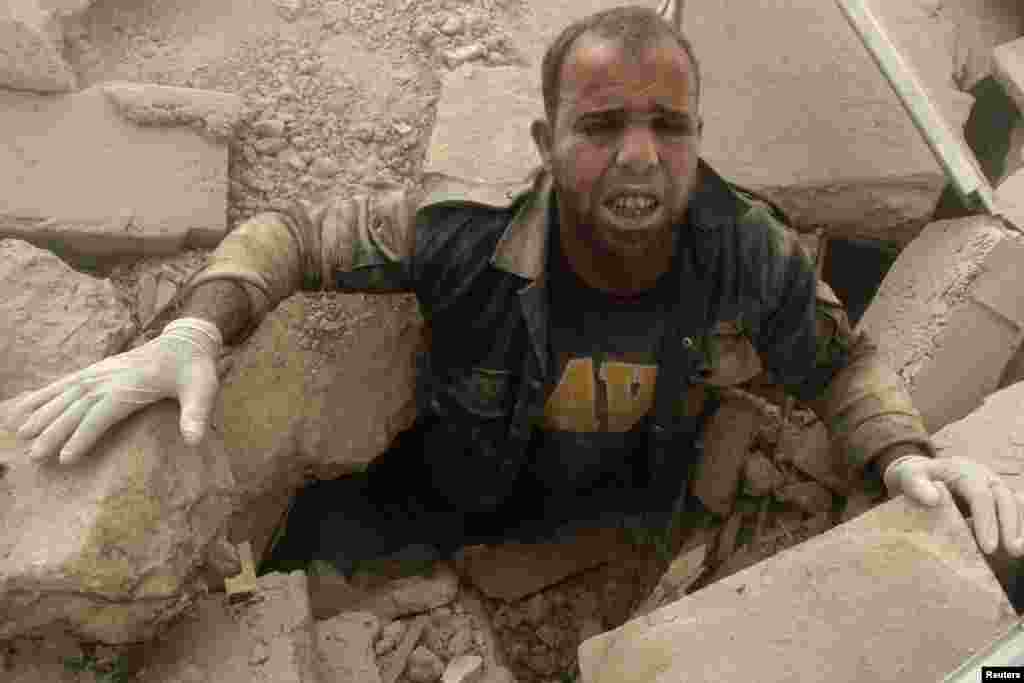 A civil defense member is stuck under debris at a site hit by what activists said were two barrel bombs dropped by forces loyal to Syria&#39;s President Bashar al-Assad in the Al-Shaar neighborhood of Aleppo.