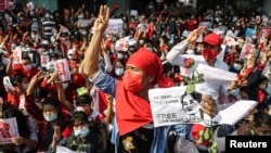 People show the three-finger salute and hold signs demanding the release of elected leader Aung San Suu Kyi as they take part in a protest against the military coup, in Yangon, Myanmar, Feb. 7, 2021