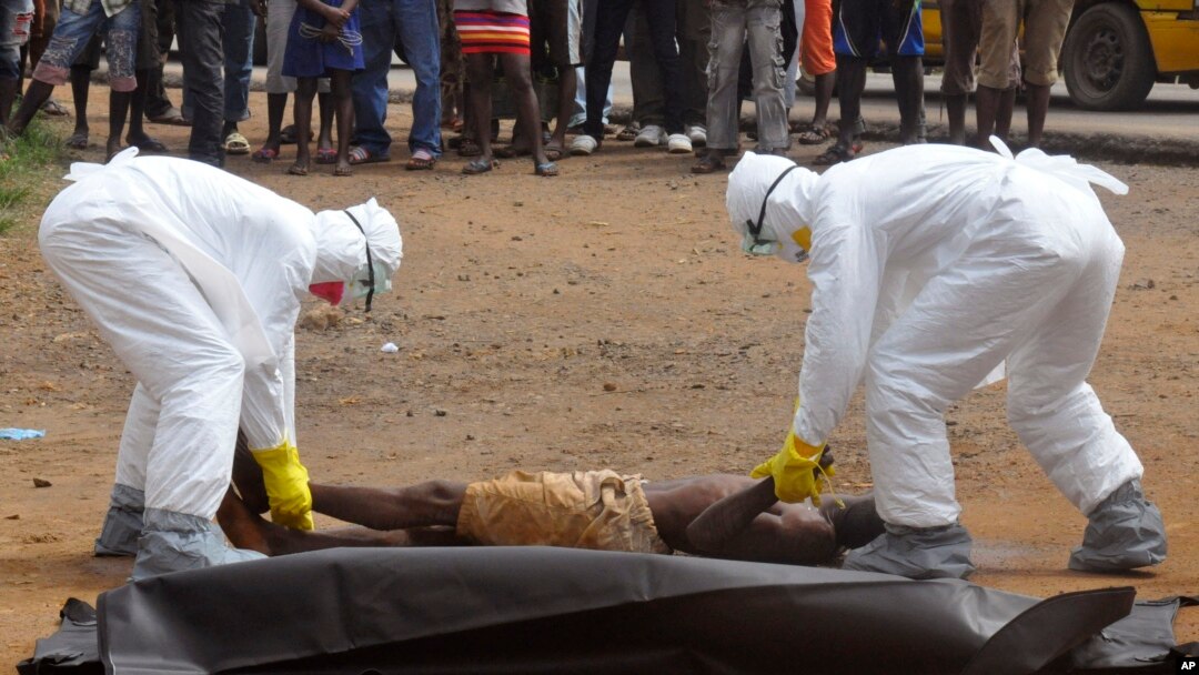 FILE - Health workers place the body of a man, whom they suspect of dying of the Ebola virus, inside a plastic body bag as a small crowd watches in Monrovia, Liberia, Sept. 4, 2014. 