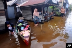 Orang-orang berbicara di luar rumah mereka di lingkungan yang terkena banjir di Banjarmasin, Kalimantan Selatan. (Foto: AP)
