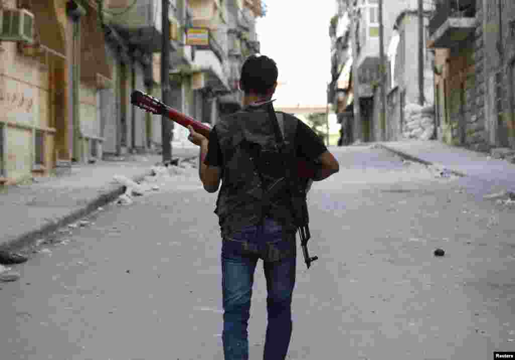 A Free Syrian Army fighter, carrying a weapon on his back, plays a guitar as he walks through a street near Aleppo September 24, 2012. 