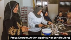 Syrian refugee Sameera Al Salam shows a colleague how to strengthen a paper handbag with glue, at an up-cycling workshop in Irbid city, northern Jordan, May 9, 2018. 