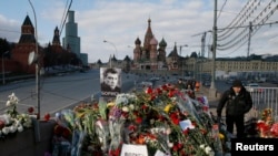 FILE - A man walks past flowers at the site where Kremlin critic Boris Nemtsov was murdered on Feb 27, 2015, at the Bolshoi Moskvoretsky Bridge, with St. Basil's Cathedral seen in the background, in central Moscow, Russia, March 6, 2015.