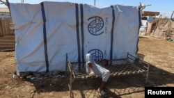 FILE - A boy displaced from Al Jazirah state due to Rapid Support Forces (RSF) violence, lies down on a bench with the logo of the International Organization for Migration behind him in New Halfa, Sudan, Nov. 2, 2024.