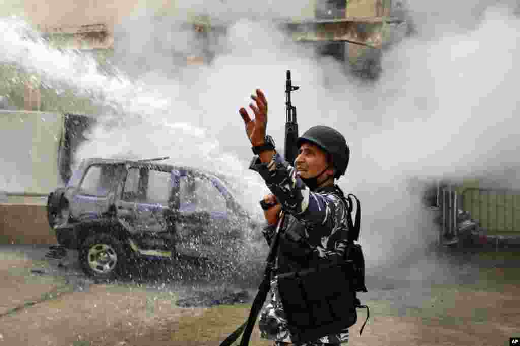 A police officer gestures to firefighters as they extinguish a police car that was set on fire by anti-government protesters in the northern city of Tripoli, Lebanon, April 28, 2020. 