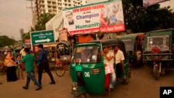 FILE - Bangladeshis crowd a tuk-tuk on a street with a billboard in appreciation of Bangladesh's Prime Minister Sheikh Hasina for sheltering Rohingya Muslims fleeing Myanmar, in Cox's Bazar, Bangladesh, Sept. 23, 2017.